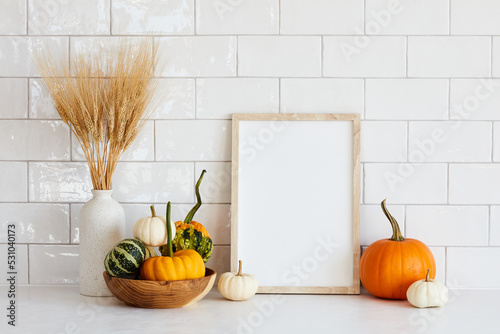 Autumn still life. Photo frame template, decorative pumpkins, vase of dry wheat on white table. Scandinavian room interior.