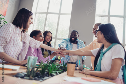 Photo of friendly cute businesspeople making arms stack teambuilding indoors workstation workshop restroom