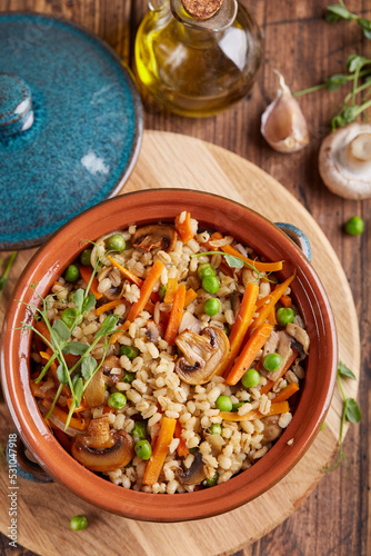 Pearl barley grain porridge with carrot, mushrooms, green peas and onion. Lenten vegetarian dish.