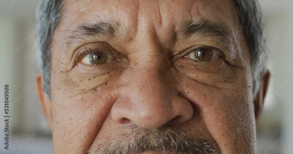 Video close up portrait of senior biracial man looking to camera and blinking in slow motion