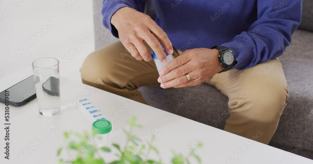 Video of midsection of senior biracial man sitting and taking pills at home Video of midsection of senior biracial man sitting and taking pills at home