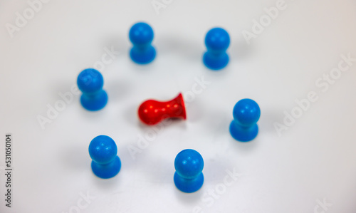 A red pawn surrounded by blue pawns symbolizing a man or woman whoi is in danger, isolated, killed, sick, in minority, different, bullied, unpopular, defeated, defenseless, wounded.