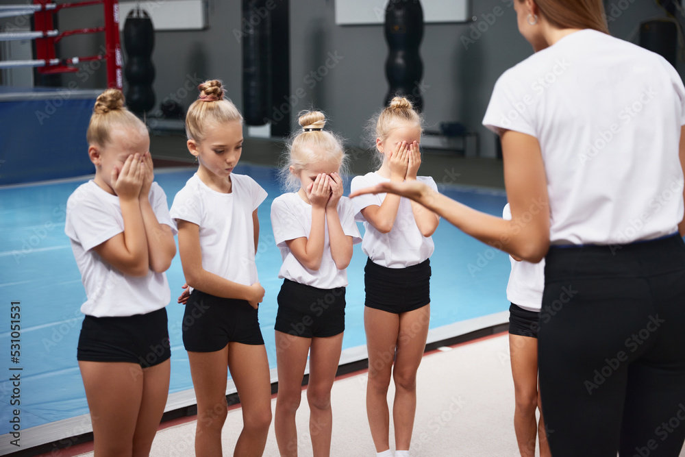 Training with coach. Young woman teaching little girls, beginner gymnastics athletes at training at sports gym, indoors. Concept of sport, achievements, studying