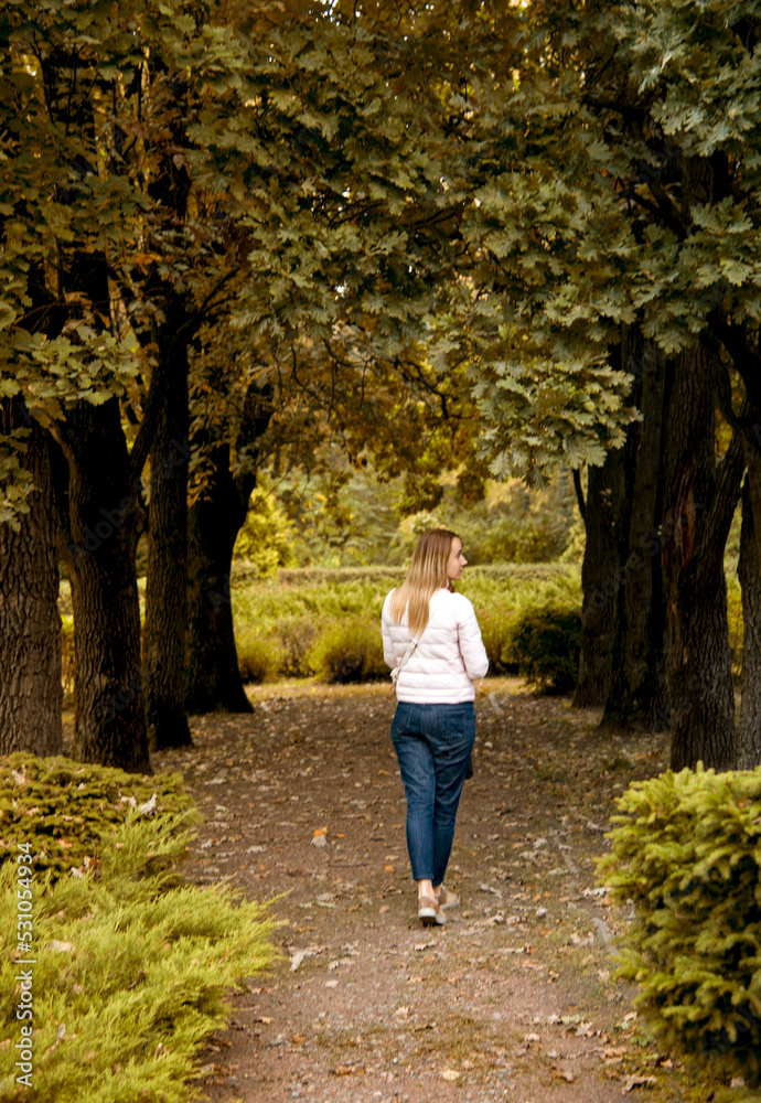 beautiful smiling girl in pink sport jacket walking in autumn park with a bouquet of autumn leaves holding in her hands