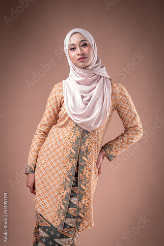 Portrait of a beautiful female model wearing traditional dress and hijab, a lifestyle apparel for Muslim women isolated on brown background. Idul Fitri and hijab fashion concept.