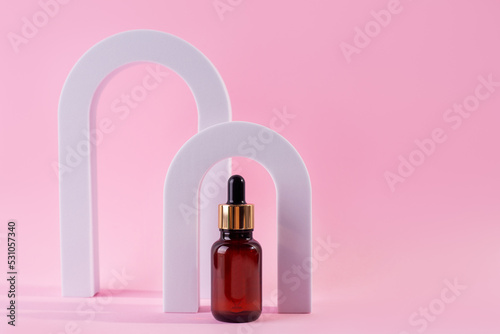 Beauty collagen face serum in a glass dropper bottle in Arch on pink background. Trendy shoot of cosmetics packaging. Essential oil with natural ingredients..