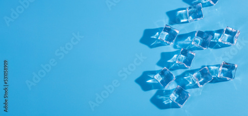 Top above overhead close up macro view photo of ice cubes and water drops on blue background with copy empty blank space.