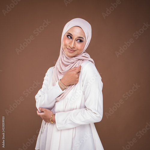 Portrait of a beautiful female model wearing hijab, a lifestyle apparel for Muslim women isolated on brown background. Idul Fitri and hijab fashion concept. © HEMINXYLAN