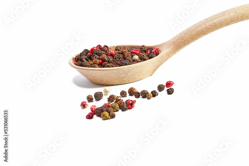 Mixture of peppers in a wooden spoon and scattered balls of pepper on a white background, seasonings, spices, kitchen