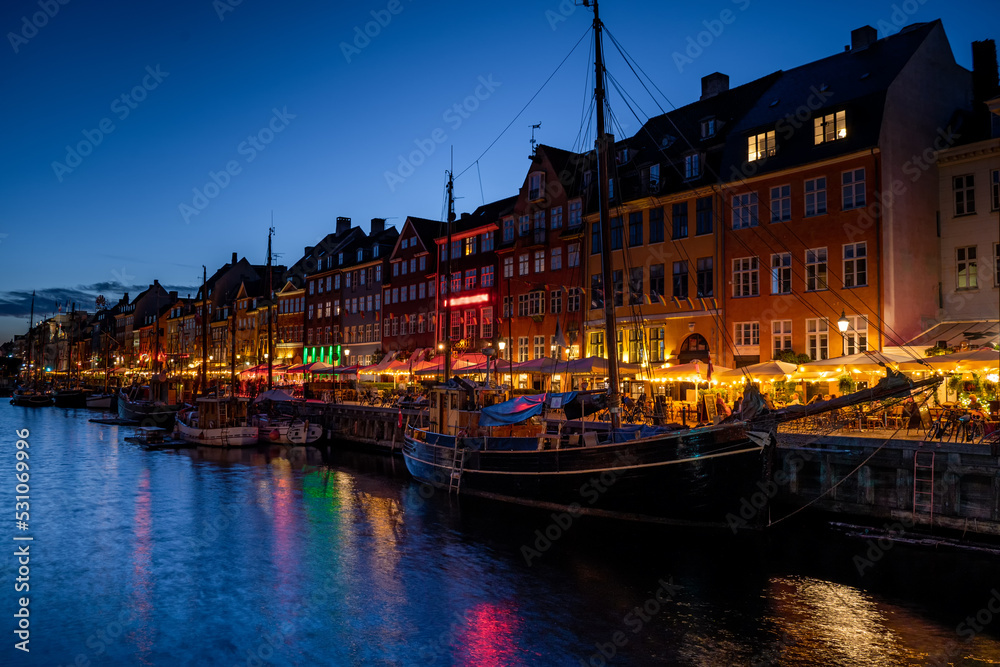 View of Nyhawn, the colorful houses next to the old port. Tourist visiting restaurants, cafes and ships in the canal at night. The most important sightseeing spot in Copenhagen, Denmark.