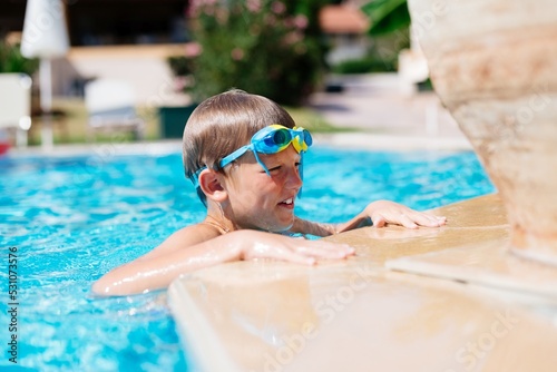 Boy with swimming goggles is resting after swimming in the pool. Happy summer vacation in Corfu, Greece