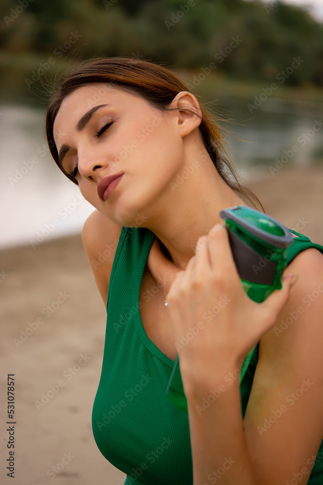 a girl in a sports uniform holds a bottle in her hand, a girl drinks water from a bottle, a girl is dressed in a green tracksuit top and cycling shorts, water balance, outdoor sports, sports lifestyle