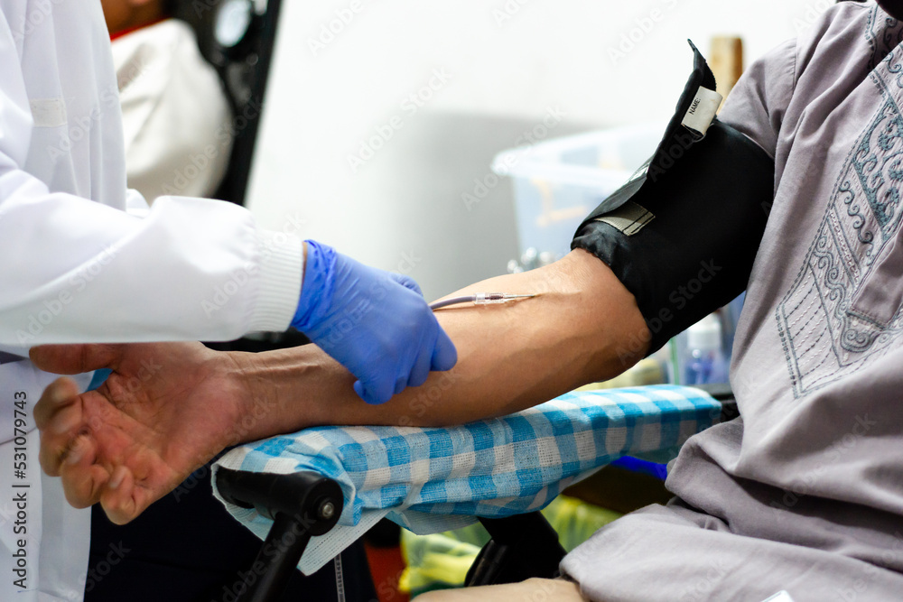 Doctor helps patient donate blood. the doctor's hand puts a needle into the blood donor's arm