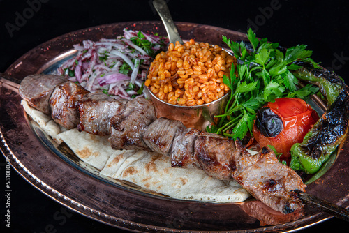 Traditional Turkish cuisine Lamb skewers on a barbecue skewer, grilled shashlik as top view on an served on a copper tray.