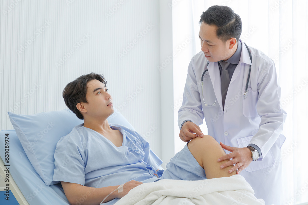 Senior doctor and young male patient who lie on the bed while checking symptom, consult and explain  in hospital wards.