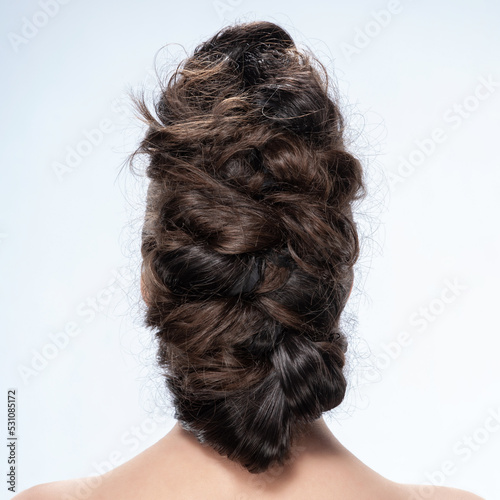 Back view of young woman. Close-up portrait of a nude young caucasian woman with curly hair. Dark hair. Stylish hairstyle. Isolated on a light