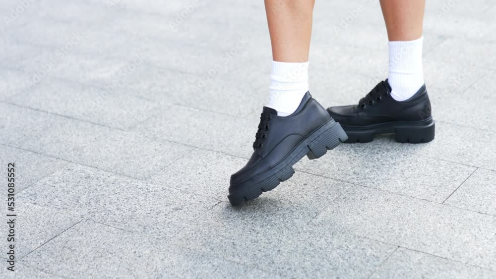 Fashionable shoes demonstration. Model in white socks wears black leather oxford boots on tractor soles with thick laces. High angle view. Fashionable shoes demonstration. Model in white socks wears black leather oxford boots on tractor soles with thick laces. High angle view.
