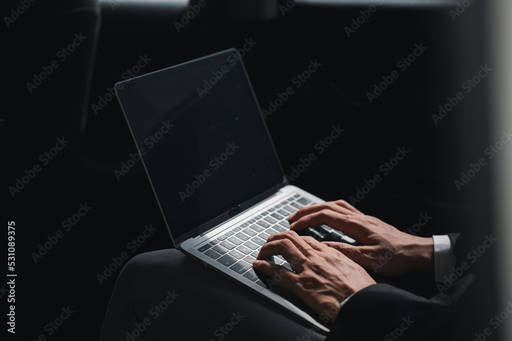 man in suit sitting in the backseat of a car, he is using his laptop to work on the go, he is on his way to work at a company with a driver, travel by car, safe driving , respecting traffic rules. man in suit sitting in the backseat of a car, he is using his laptop to work on the go, he is on his way to work at a company with a driver, travel by car, safe driving , respecting traffic rules.