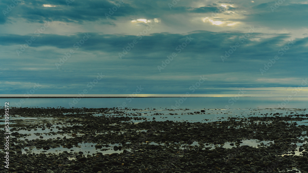 Clouds over ocean horizon as seen from a pebble beach at dawn.