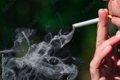 Man smoking cigarette at summer day,closeup.Blurred outdoors green background.