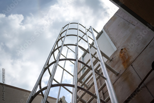 An emergency way climbing ladder with falling prevetion cage at the outside of factory building. Industrail equipment object photo, selective focus at some rail step. photo