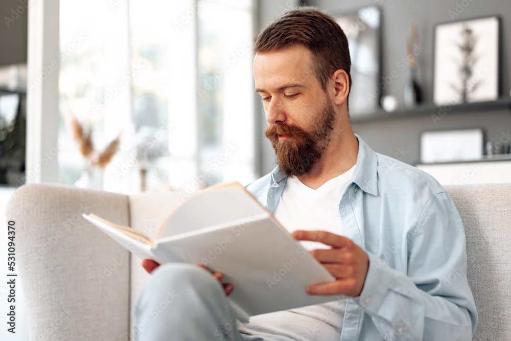 Young bearded handsome man reading book on couch at home Young bearded handsome man reading book on couch at home