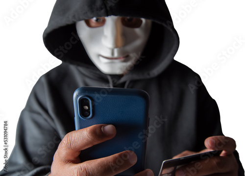 An anonymous masked hacker is using a smartphone to penetrate credit card financial information with clipping path. Hacking and malware concept.