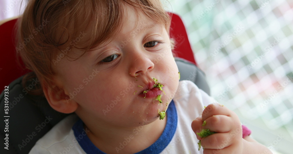 Baby eating blueberries sitting on sofa. Infant one year old toddler eats healthy snack