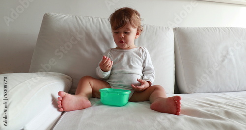 Baby eating afternoon snack on couch. Calm one year old toddler boy resting on sofa