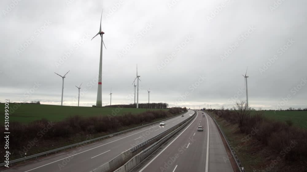 High angle shot of an industrial windmill farm on a cloudy wet day with a busy highway cutting through the shot. High angle shot of an industrial windmill farm on a cloudy wet day with a busy highway cutting through the shot.