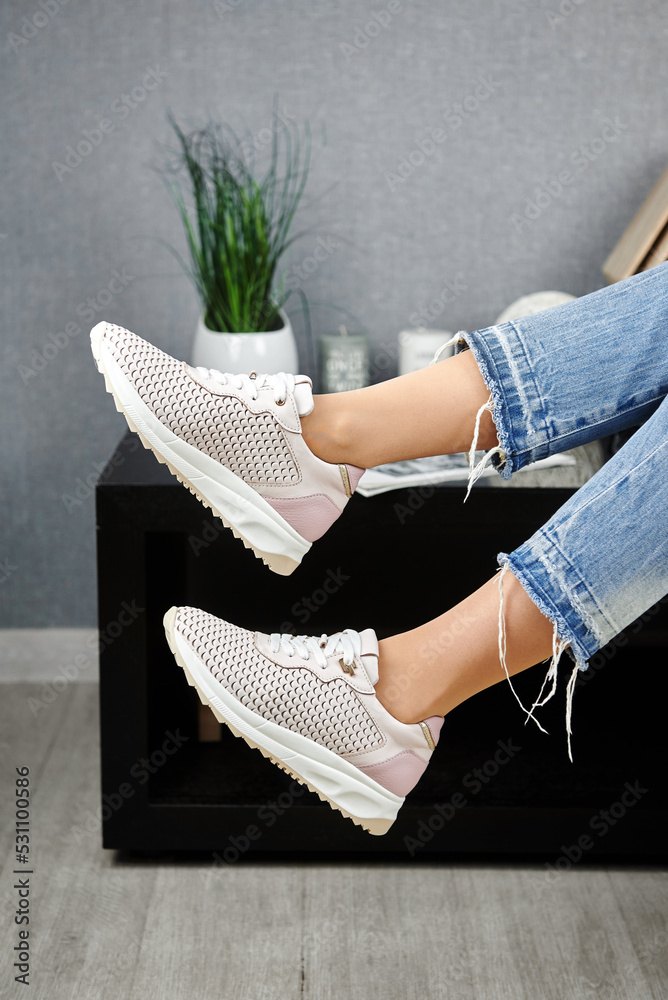 Φωτογραφία Young woman in blue jeans trying on beige sport shoes in shop, copy space