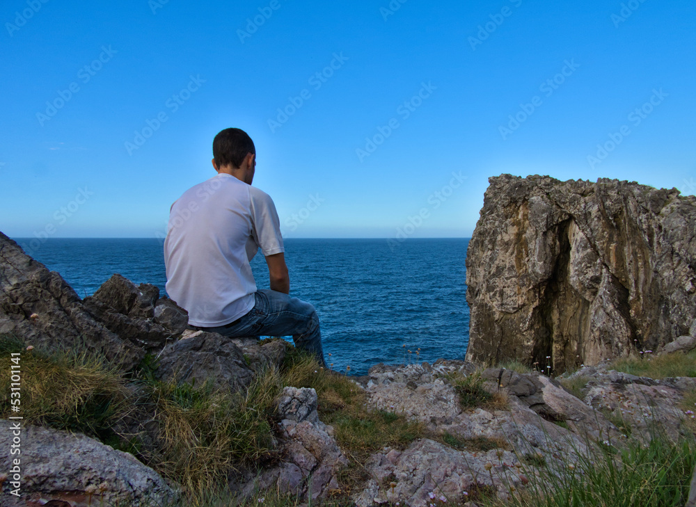 Young man sitting on the edge of a cliff thinking and looking at the sea