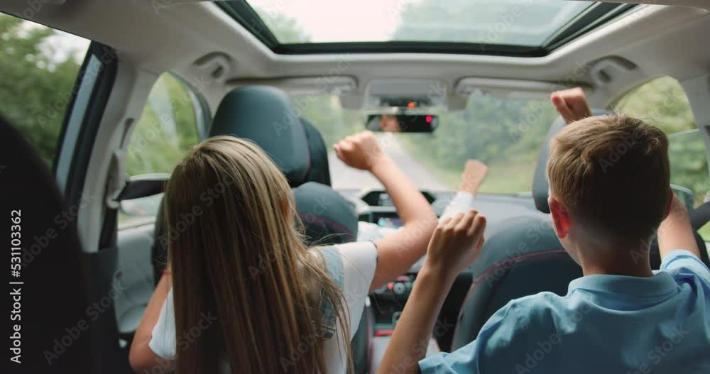 Two little boy and girl listens enjoys music and dancing while road trip. Children are playing in the car. Concept of journey.