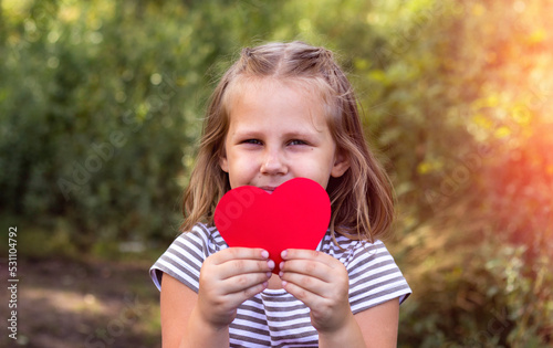 A child with a paper heart in his hands. Congratulations on Valentine's Day. copy space. Portrait of a cute little girl in the park outdoors. Love concept.
