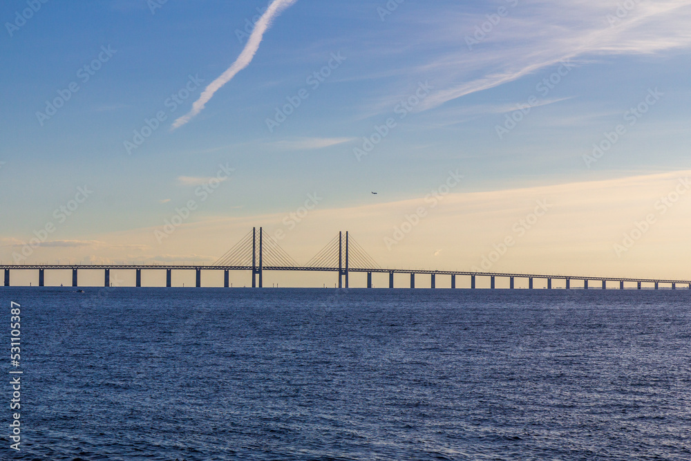 Fototapeta premium The Öresund bridge connecting Denmark and Sweden while a plane flies above it during summer sunset