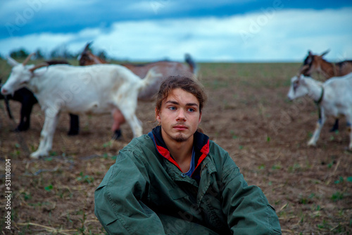 A teenage boy grazes goats in a field. A shepherd with goats in a field against a stormy sky. The concept of animal husbandry, survival, household.