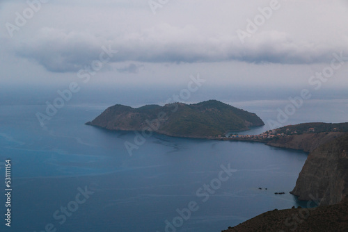Top view at Asos village and Assos peninsula during bad weather conditions, thunderstorm and rain, with low dark clouds and visible currents at sea. Cephalonia, Greece.