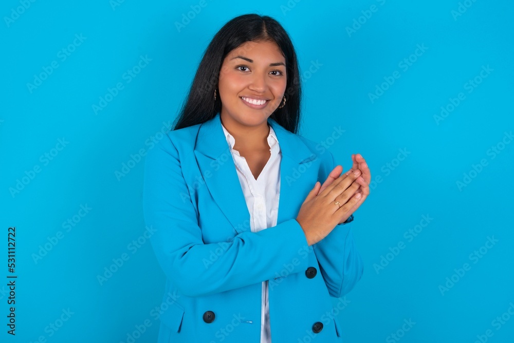 Young latin woman wearing blue blazer blue background clapping and applauding happy and joyful, smiling proud hands together. Young latin woman wearing blue blazer blue background clapping and applauding happy and joyful, smiling proud hands together.