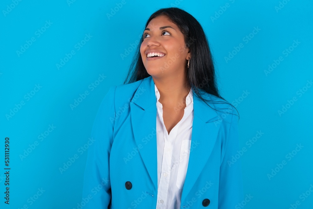 Young latin woman wearing blue blazer blue background very happy and excited about new plans. Young latin woman wearing blue blazer blue background very happy and excited about new plans.