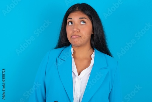 Young latin woman wearing  blue blazer blue background making grimace and crazy face, screaming out of control, funny lunatic expressing freedom and wild.