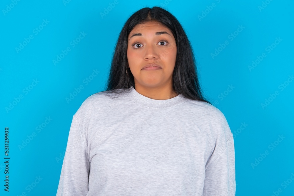 Stunned Young latin woman wearing gray sweater blue background stares reacts on shocking news. Astonished woman holds breath Stunned Young latin woman wearing gray sweater blue background stares reacts on shocking news. Astonished woman holds breath