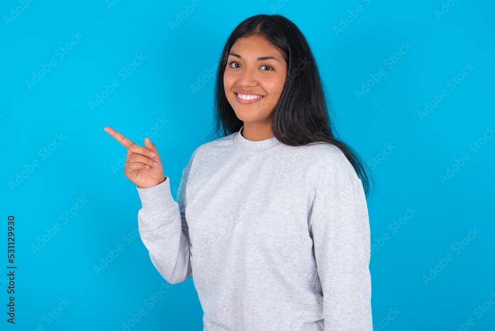 Profile photo of Young latin woman wearing gray sweater blue background indicate finger empty space offer Profile photo of Young latin woman wearing gray sweater blue background indicate finger empty space offer