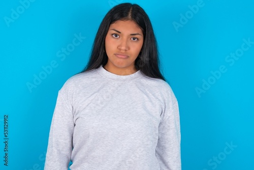 Young latin woman wearing gray sweater blue background depressed and worry for distress, crying angry and afraid. Sad expression.