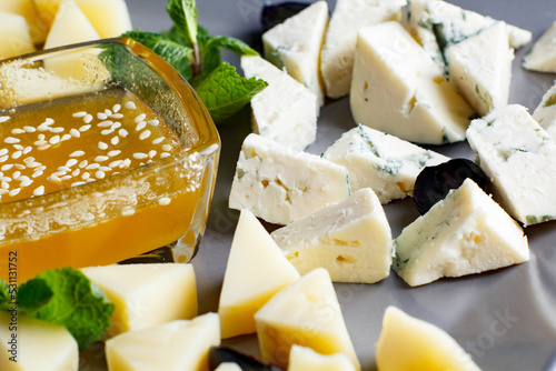 four types of cheese, feta, gorgonzola, parmesan, hard cheese, with honey on a plate, four types of cheese on a gray plate and black background