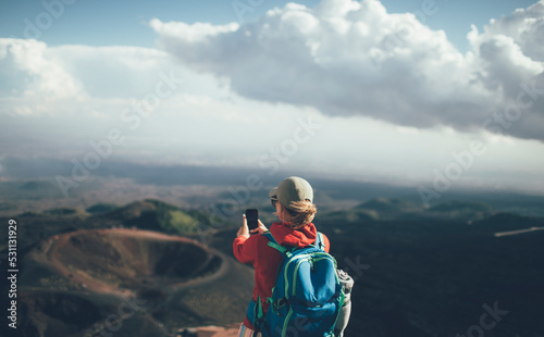 Rear view of woman backpacker taking photo with smart phone