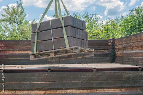 Unloading paving slabs from a truck. Men unload paving slabs using a manipulator. Workers unload building materials from a large machine.