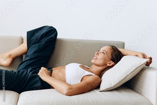 Woman with tanned skin smiling and looking at camera while lying on sofa at home