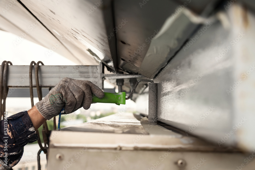 Industrial worker in uniform painting in hard reach place paint roller
