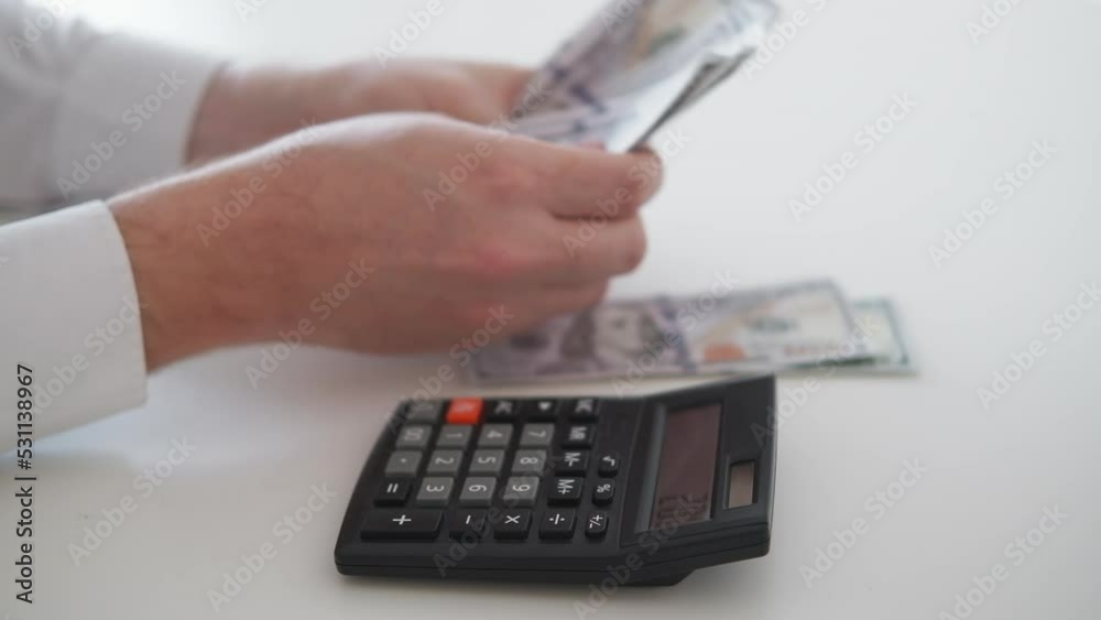 Budget money. Counting man. Payment spending. Unrecognizable guy using calculator spreading cash dollars on piles sitting light room interior. Budget money. Counting man. Payment spending. Unrecognizable guy using calculator spreading cash dollars on piles sitting light room interior.