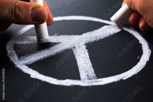 Hands drawing peace symbol with white chalks on blackboard